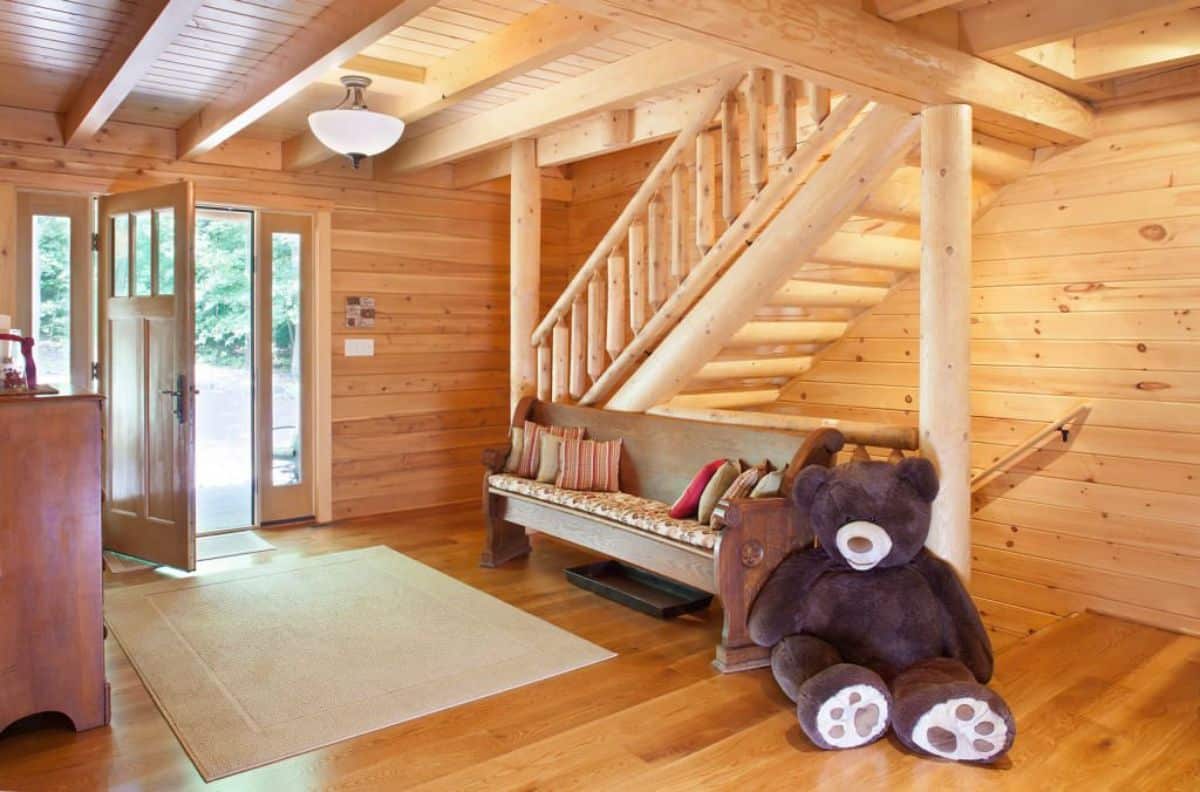 open front door into log cabin with sofa by door against stairs