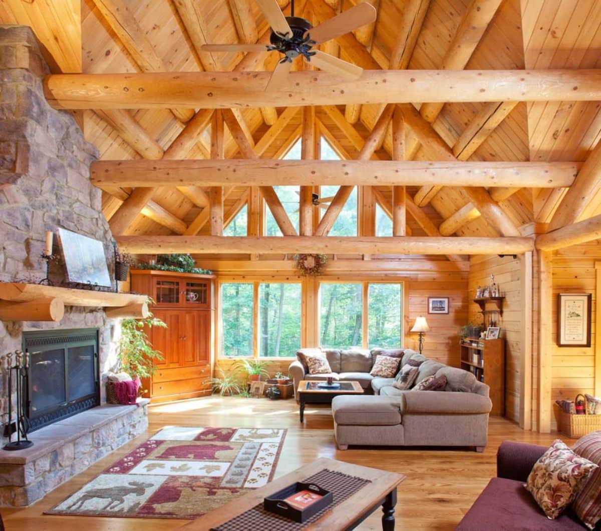 stone fireplace on left of room with light brown sofa against great room wall of windows