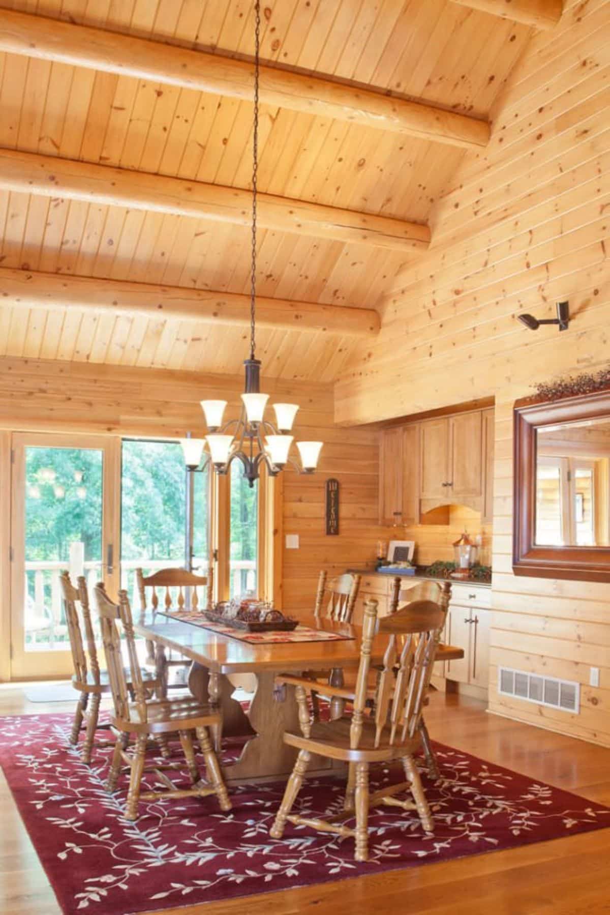 wood dining table with high back spindle chairs under simple chandelier with sliding glass door to deck on back