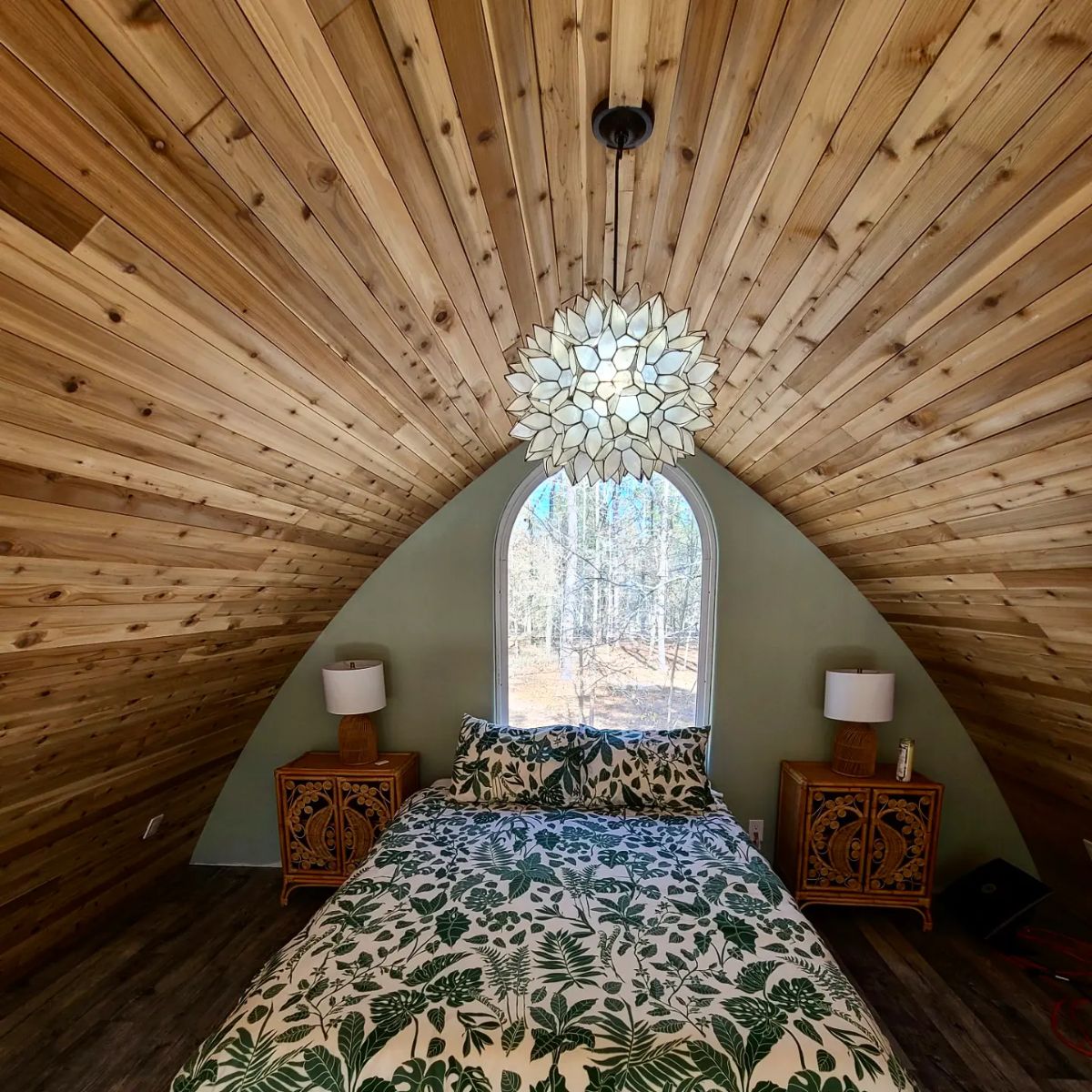 floral bedding on loft bed with curved wooden ceiling and window at back wall