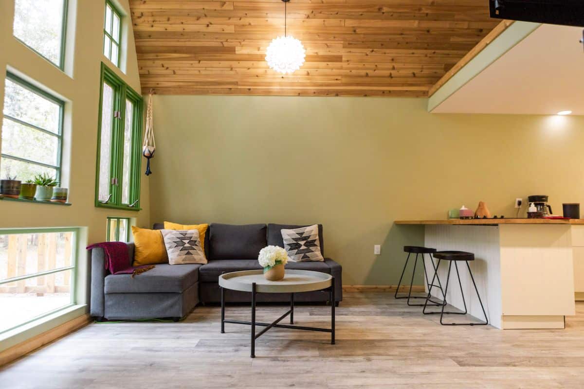 gray sofa in corner of living space with stools against bar on right