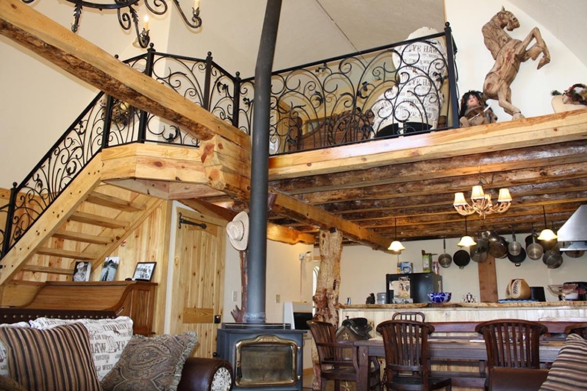 wood stove in the middle of log cabin with iron railing on loft