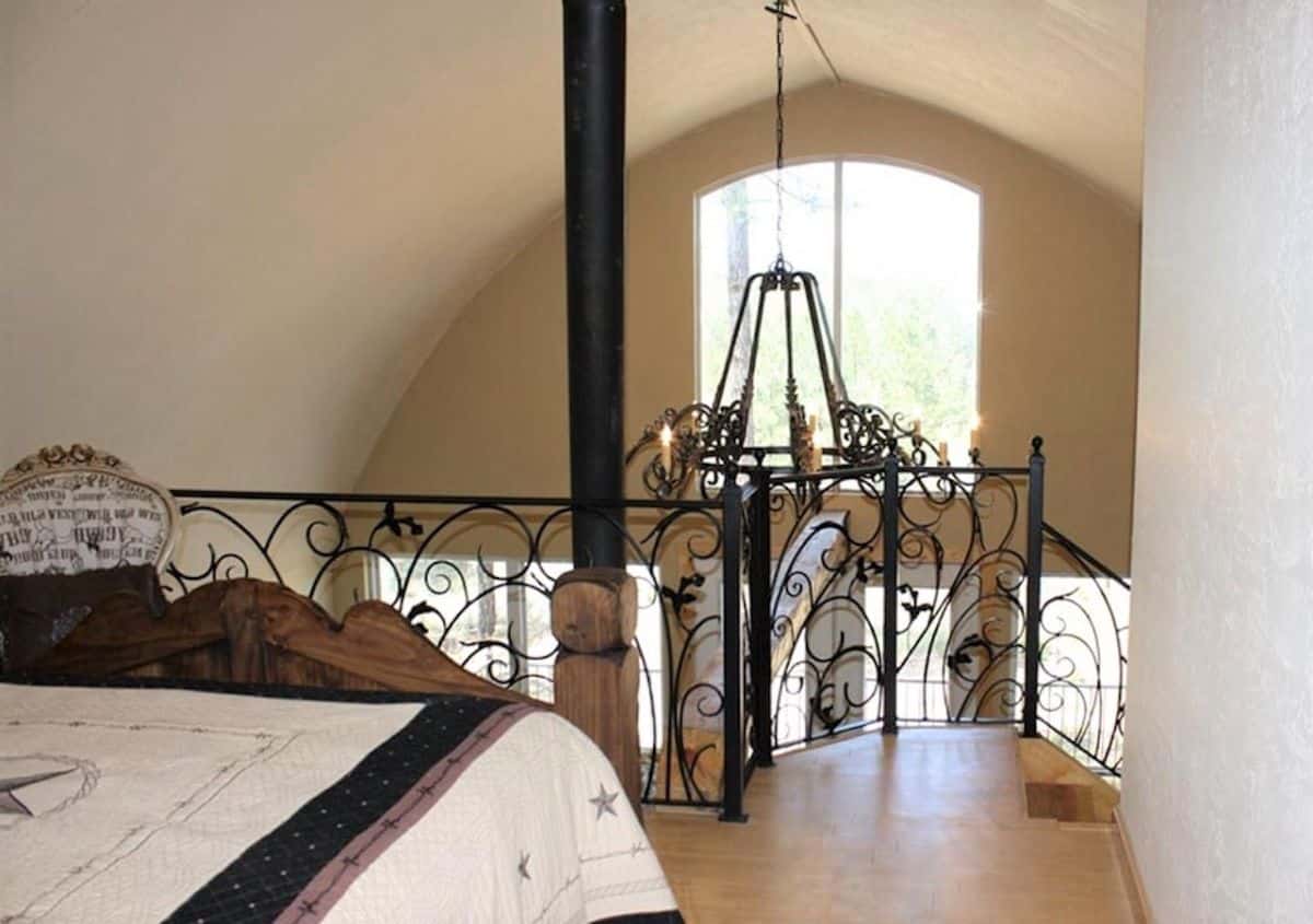 ornate chandelier hanging over living area past wrought iron railing of loft