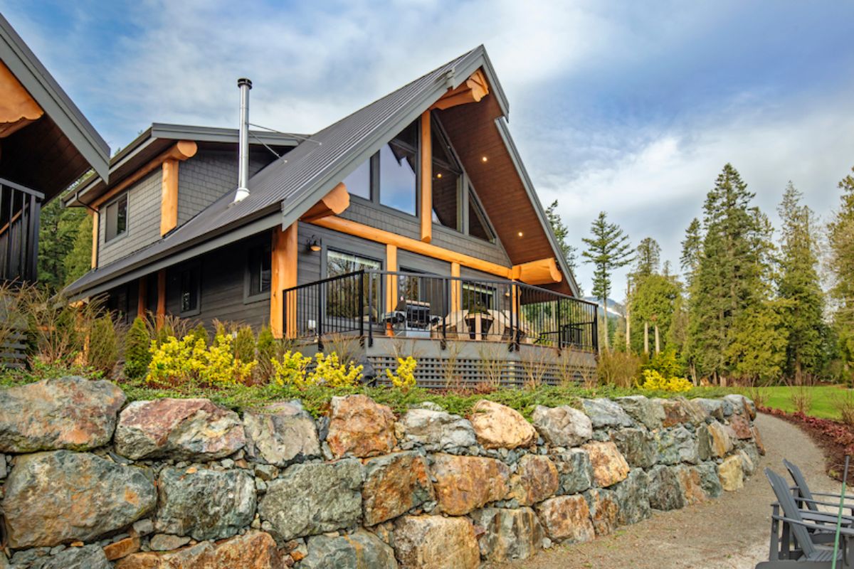 wood and gray siding on cabin with wrought iron railing on edge by rock hill