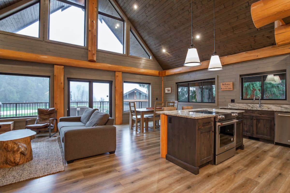 wall of windows on back side of living area with gray sofa on left and kitchen island on right