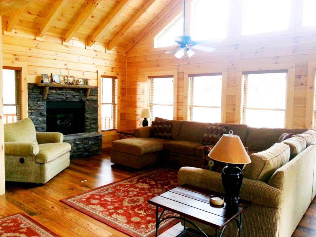 dark stone fireplace on left with brown sofas against wall of windows