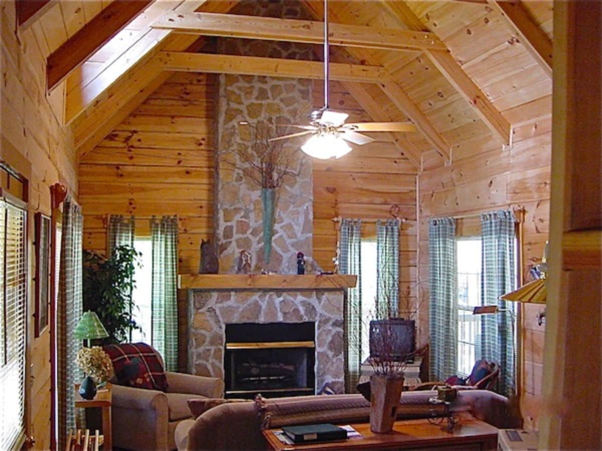 stone fireplace in living area of log cabin with sofas in foreground