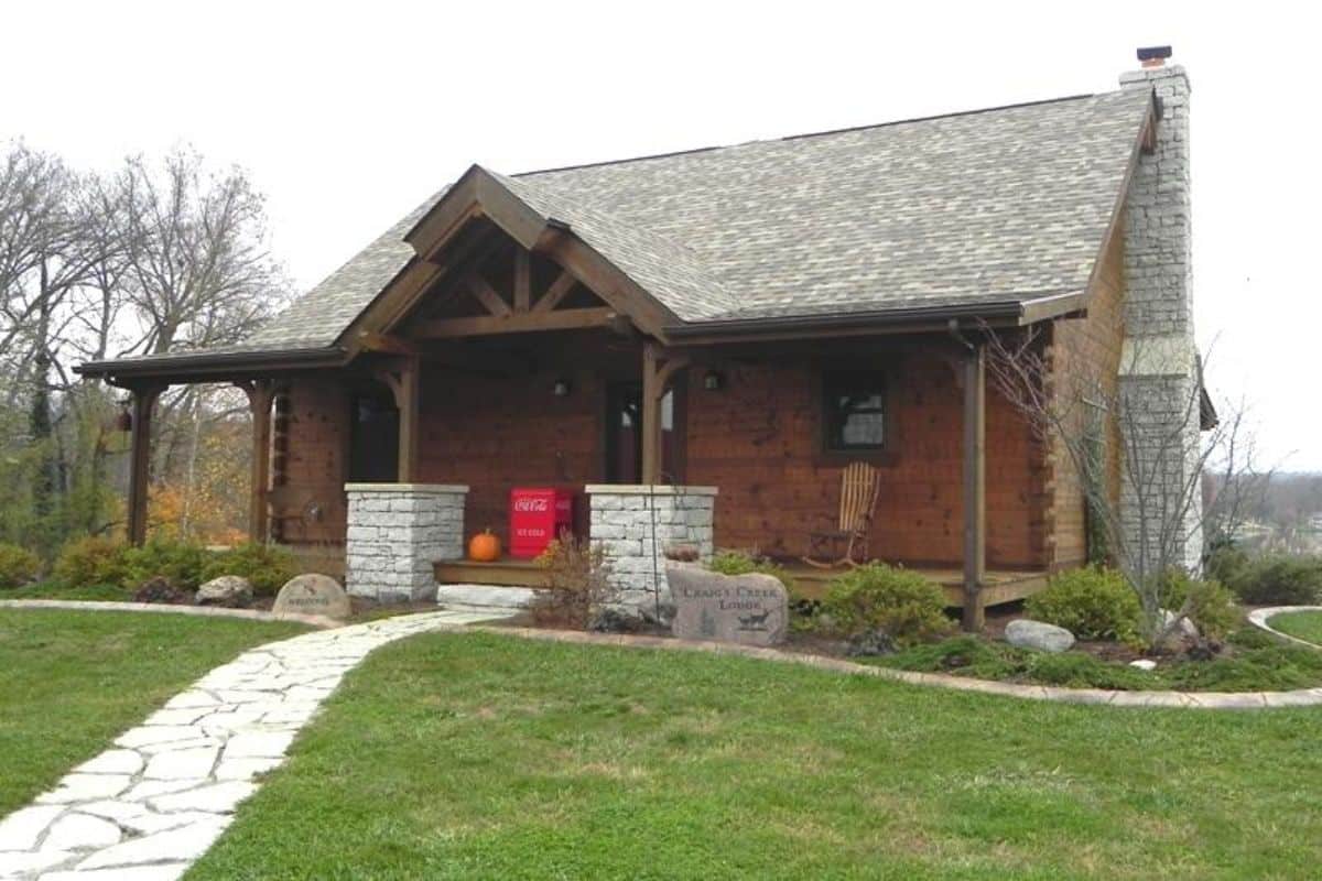 dark wood cabin with gray roof and stone path to front porch