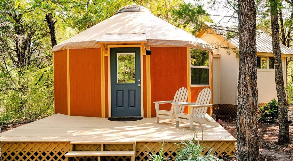 blue door on front of orange yurt with cream roof and deck around base