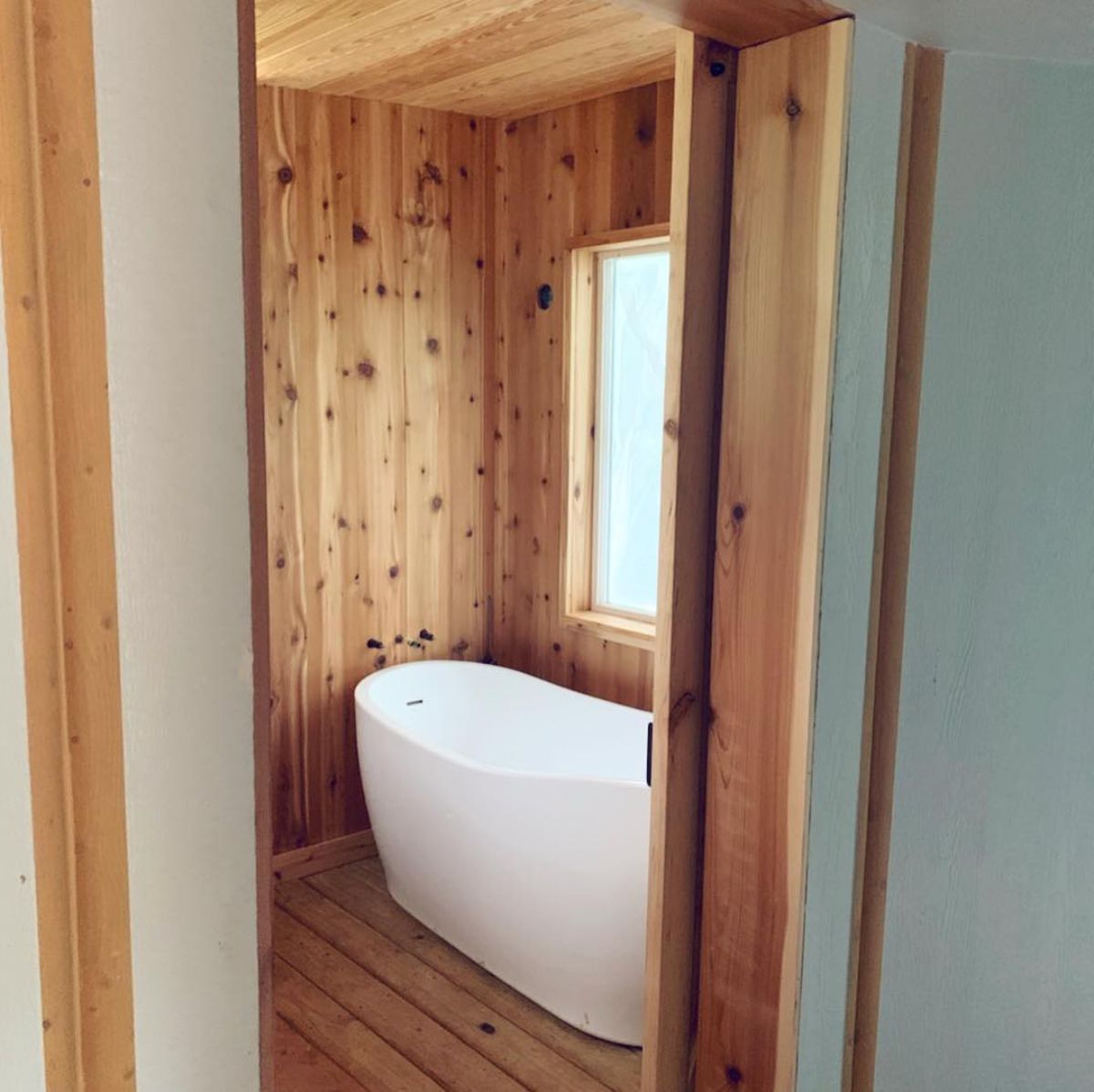 white soaking tub inside bathroom with wood walls