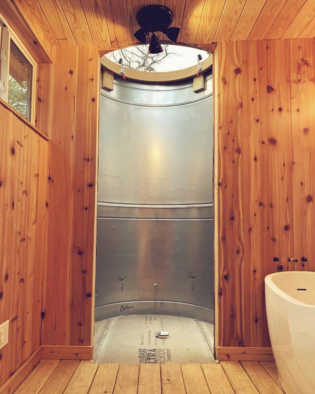 corrugated metal round shower at end of bathroom with white bathtub on right