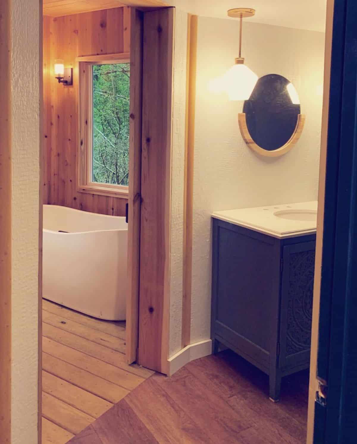 view of black cabinet with white counter and sink just outside door to bathroom with soaking bathtub under window