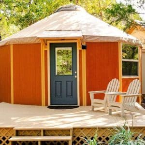 blue door on front of orange yurt with cream roof and deck around base