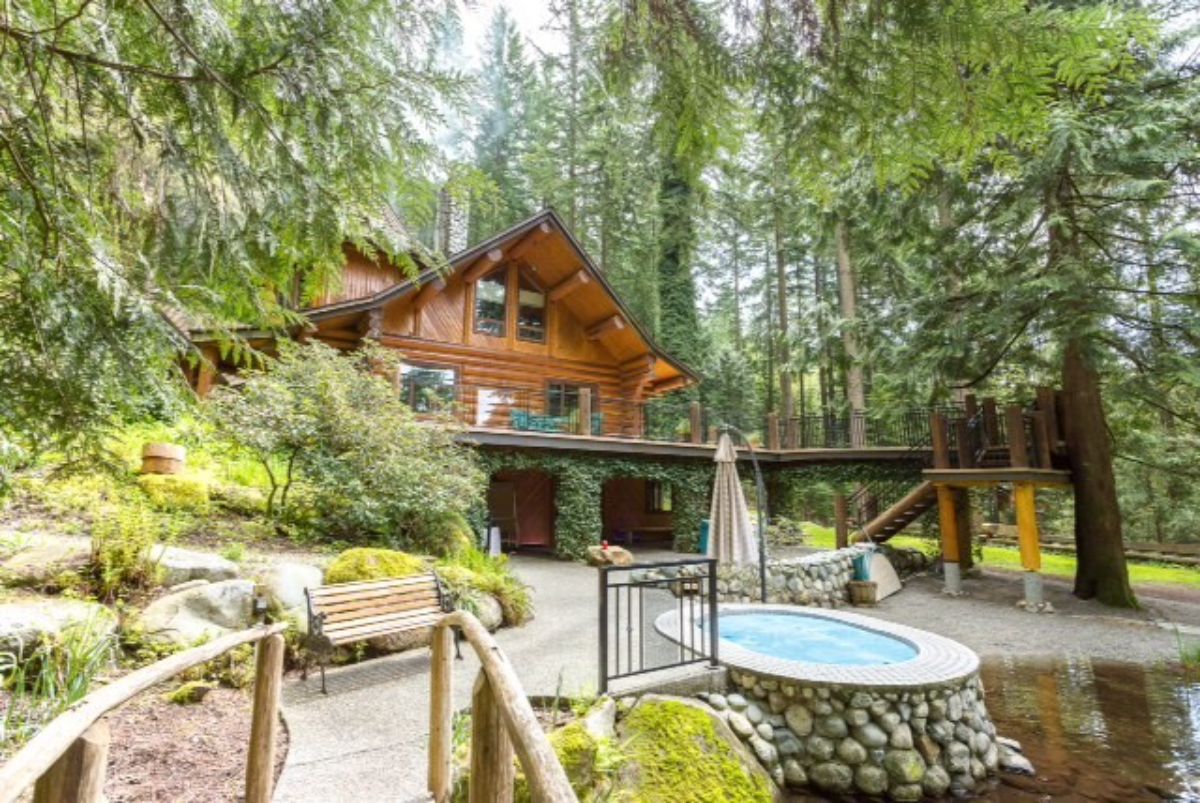 walkway with wood railing and small jacuzzi on edge of pond behind log cabin