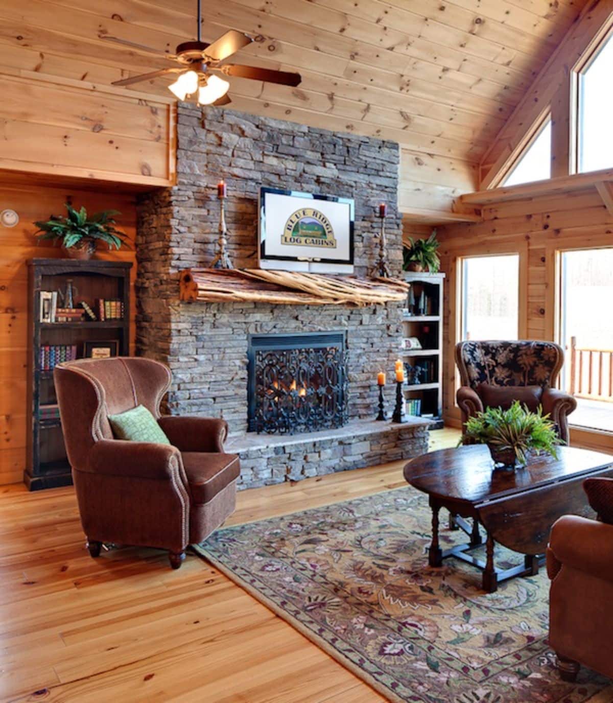 stone fireplace against wall in living room with brown chairs and windows on right