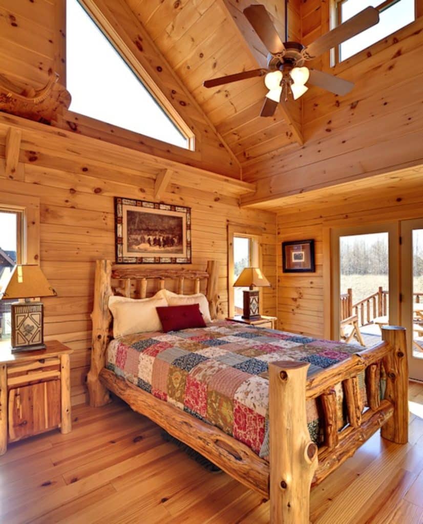 bedroom with wood bed frame and quilt on bed alongside doors to deck