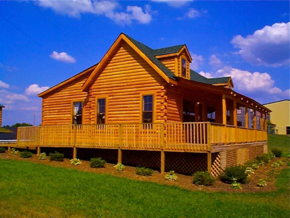 side of log cabin with open wrap around porch and two windows