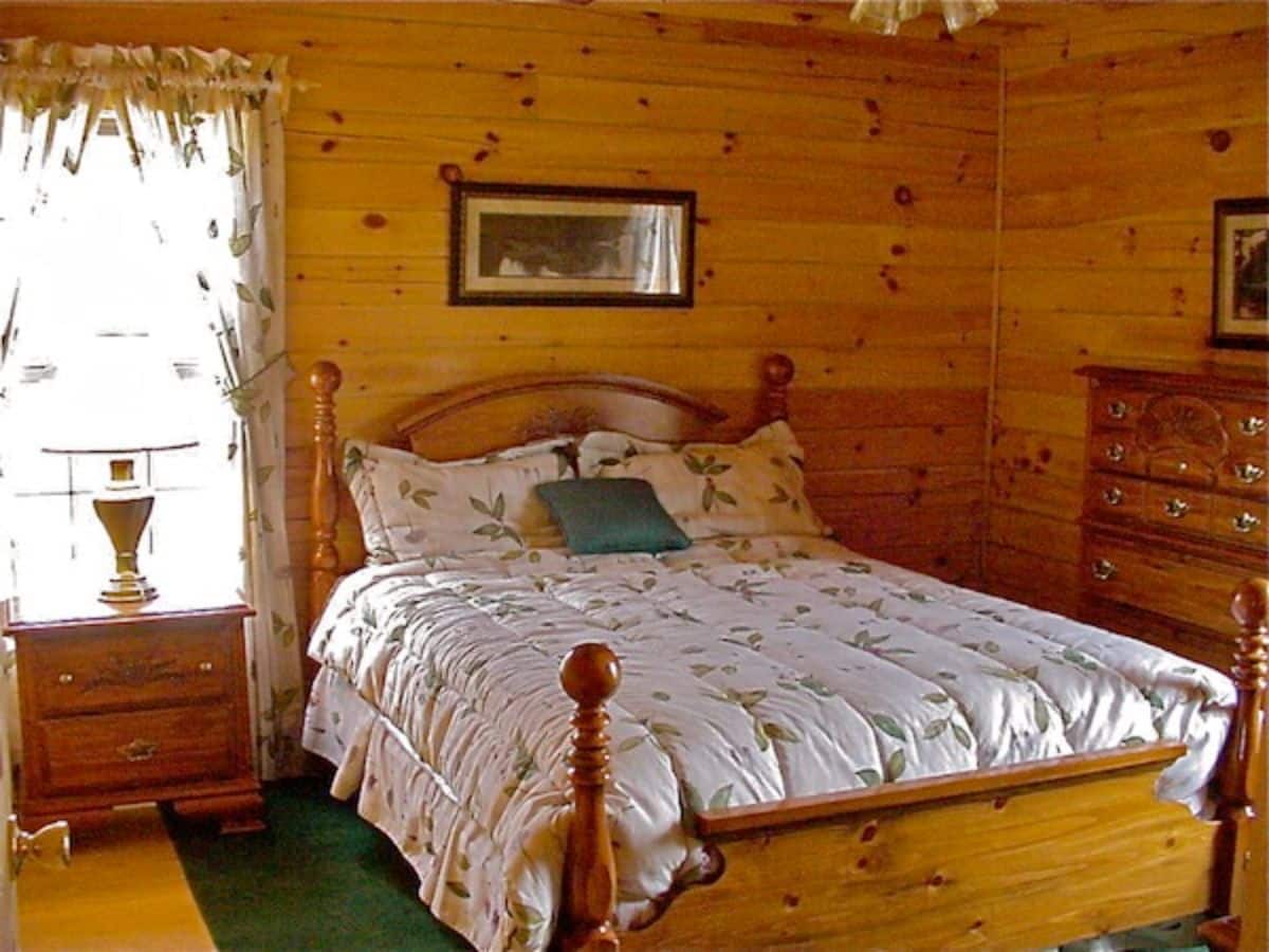 white linens on wood bedframe in room with green carpet rug