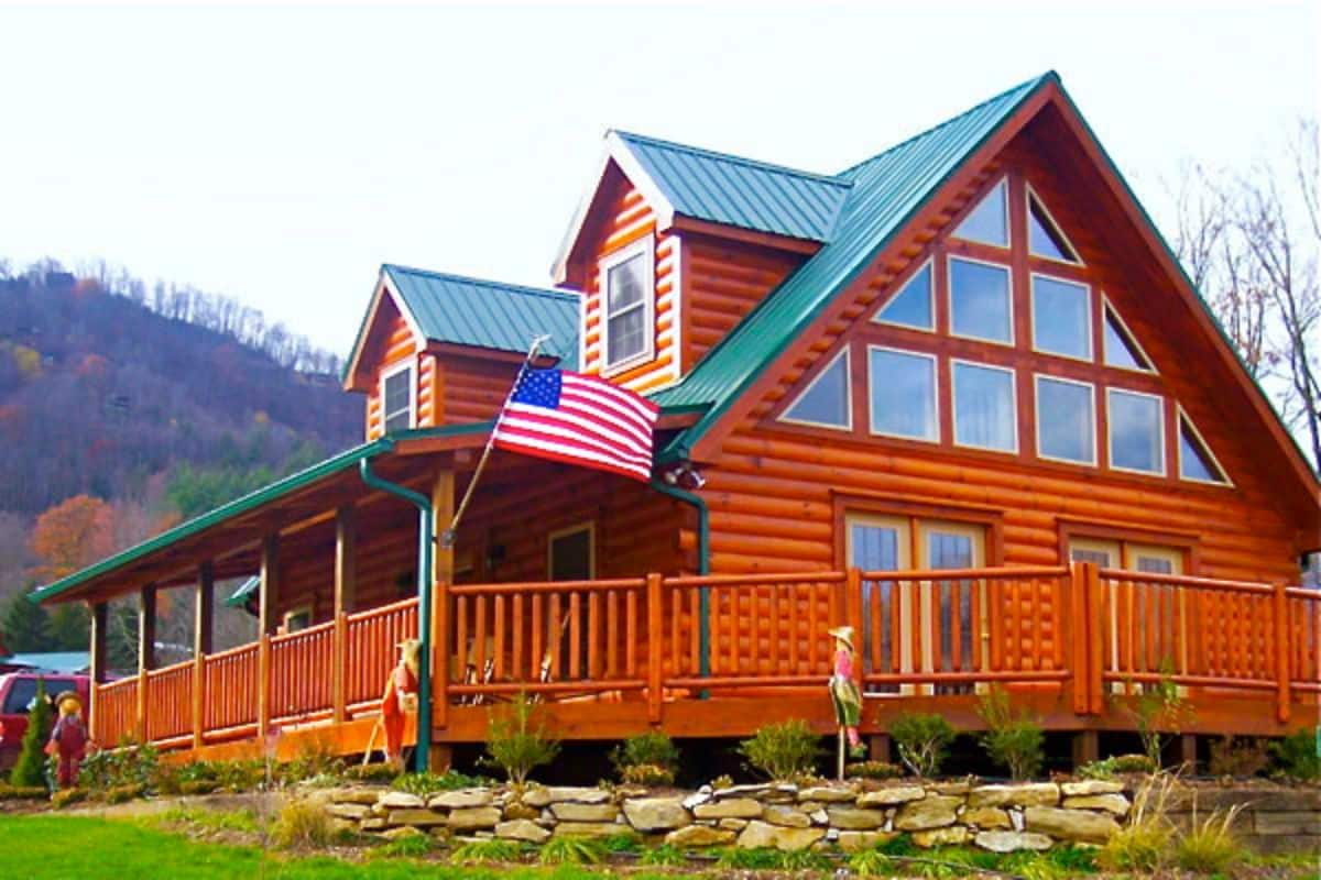 log cabin with medium wood stain green roof and american flag hanging on porch