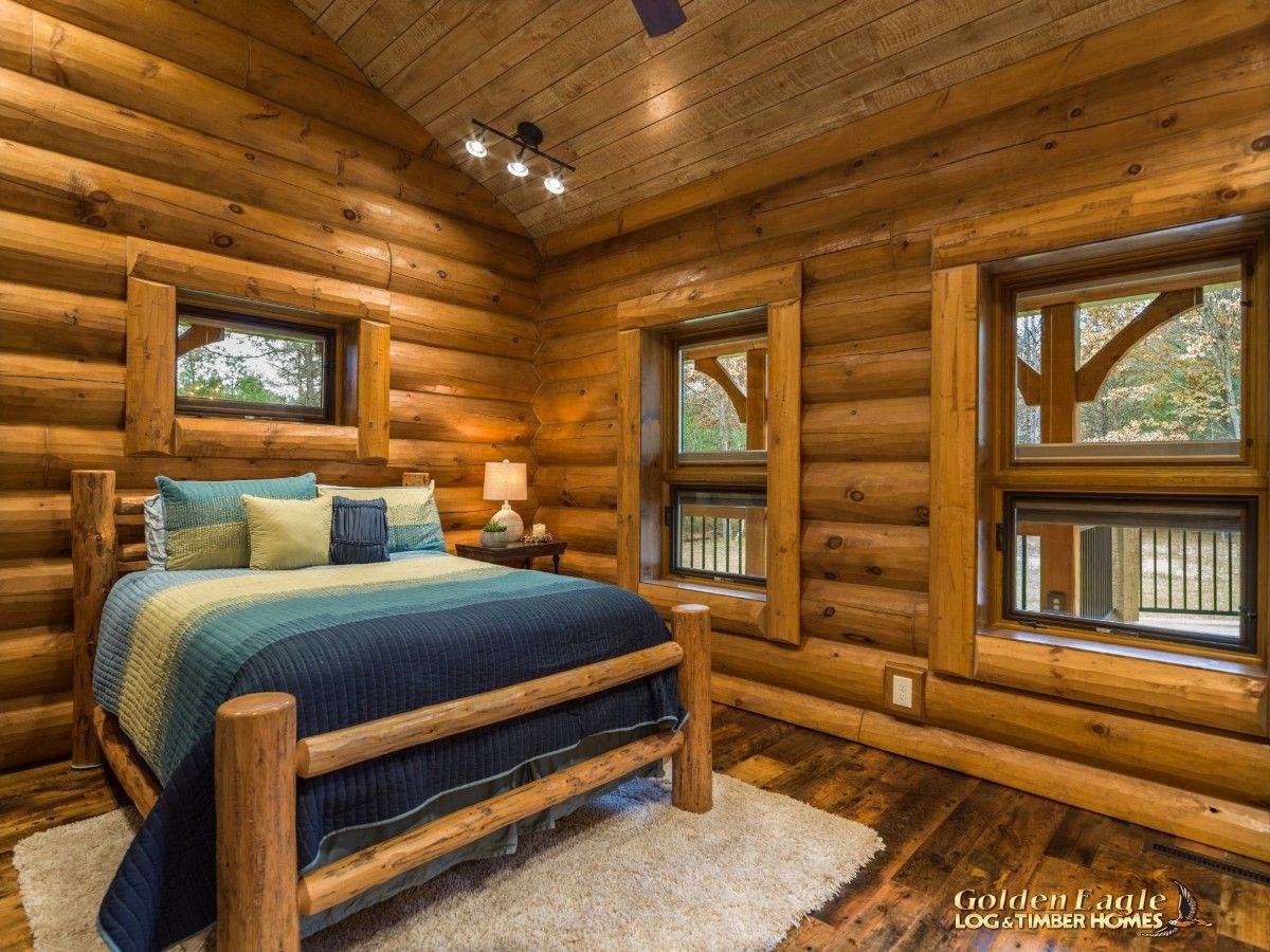 blue bedding on log bedframe in log cabin bedroom with windows on all sides