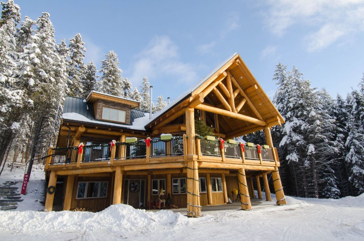 light wood log cabin with covered upper deck porch and snow on ground