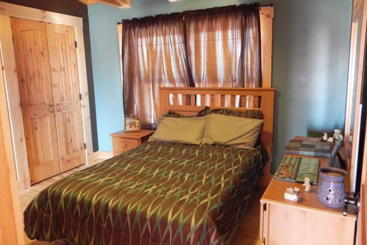 dark green bedding on wood bed against curtained windows in cabin with blue wall
