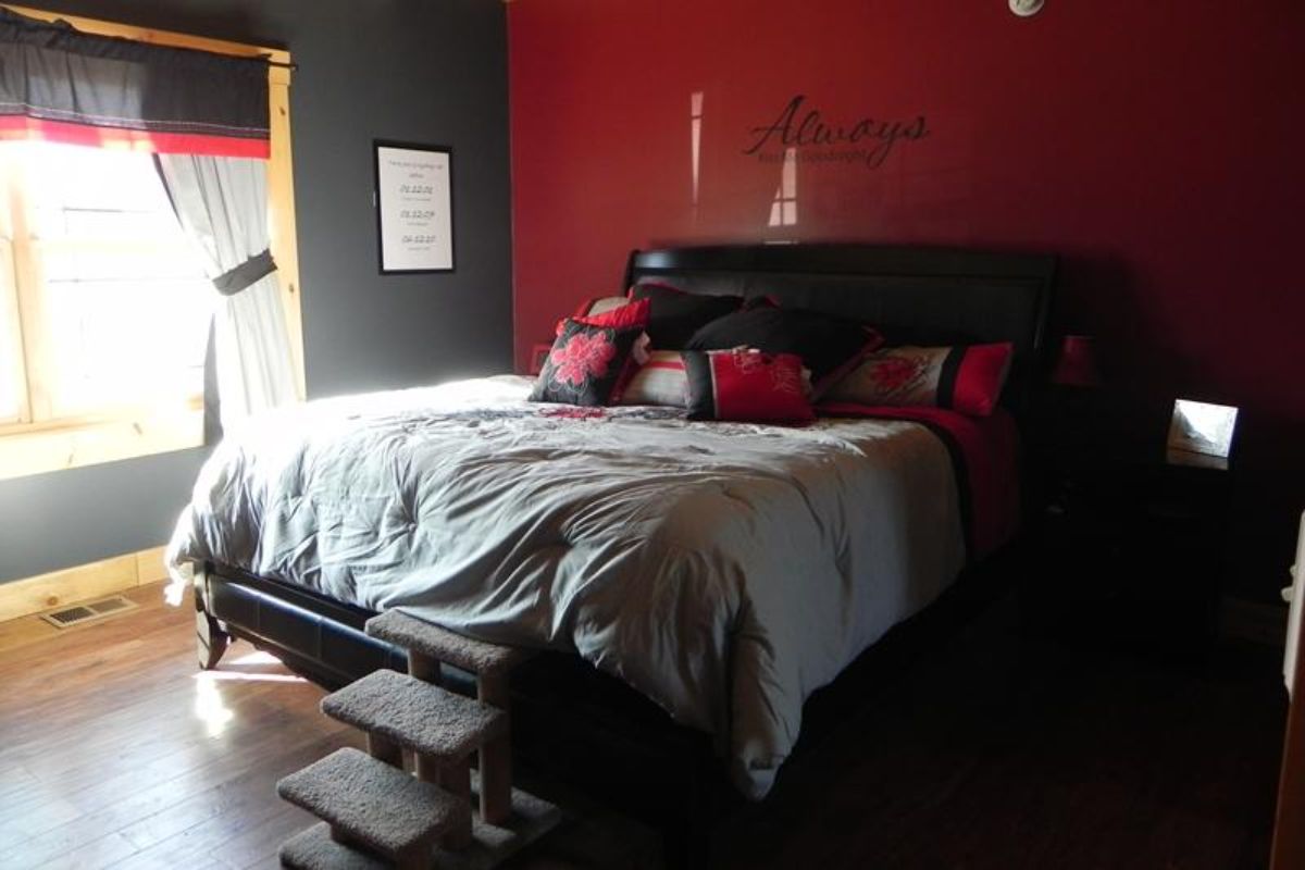 gray bedding on black bed against dark red wall