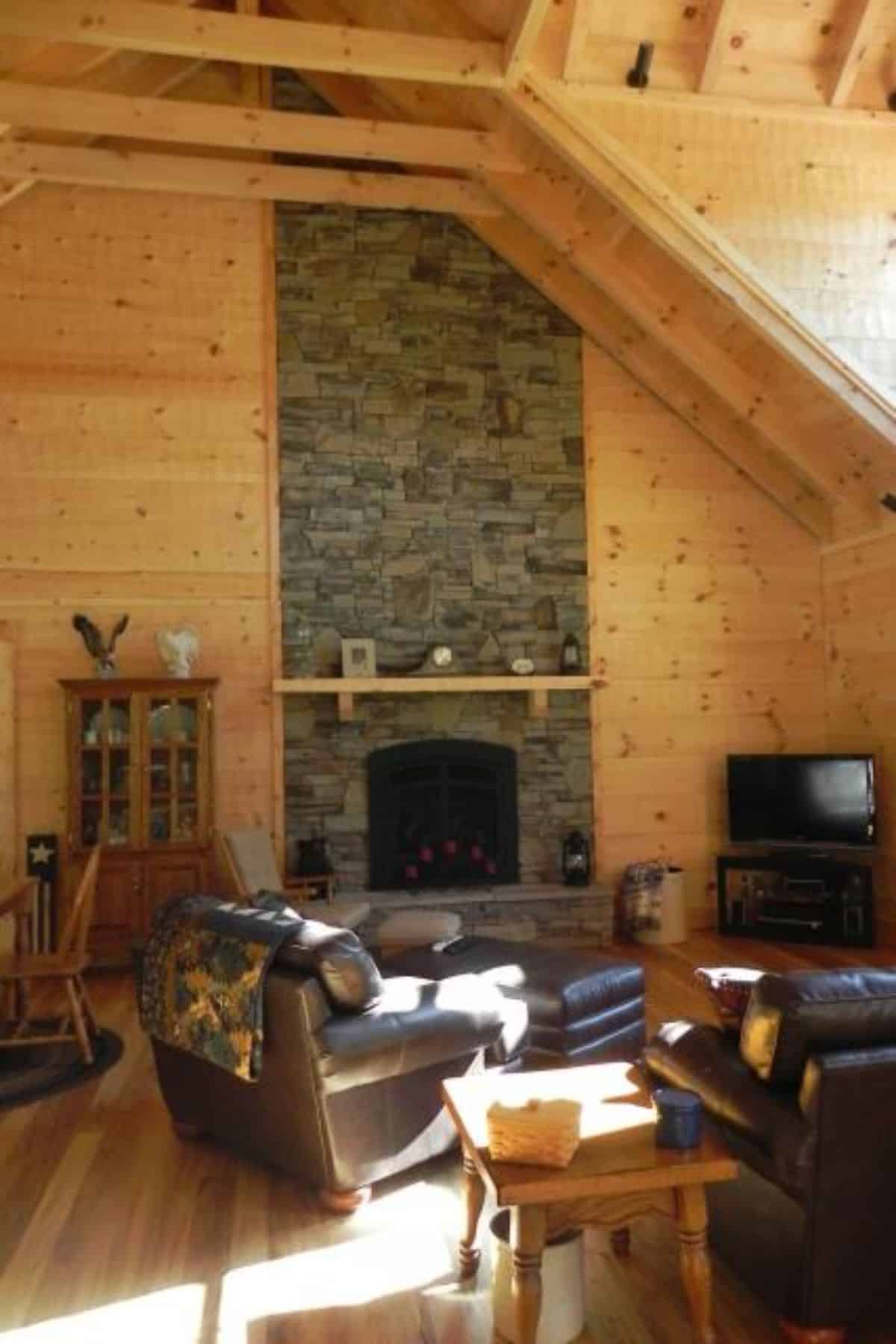 stone fireplace against back wall of log cabin with leather chairs in foreground