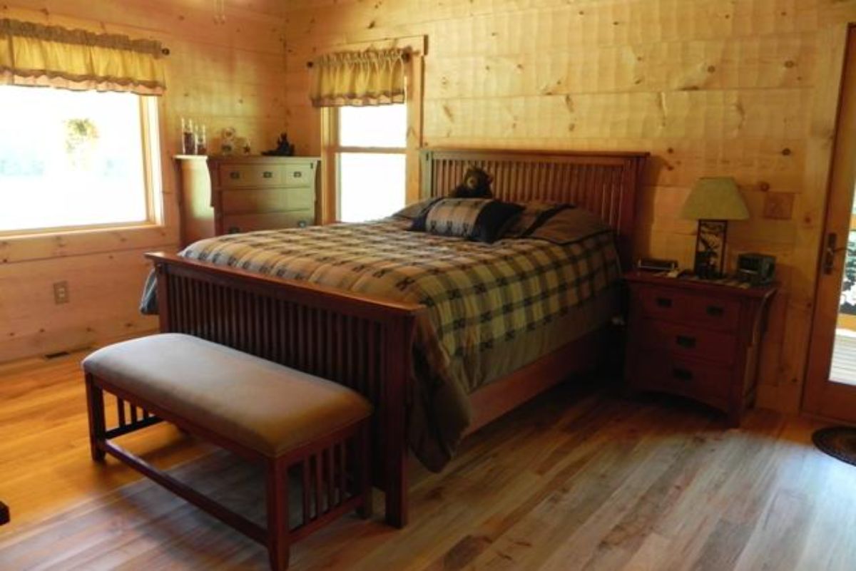 wood bed frame on bed in light wood walled bedroom