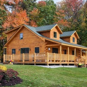 light wood cabin with dormer windows and wrap around open porch