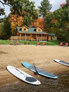 view of log cabin from beach with paddle boards in foreground