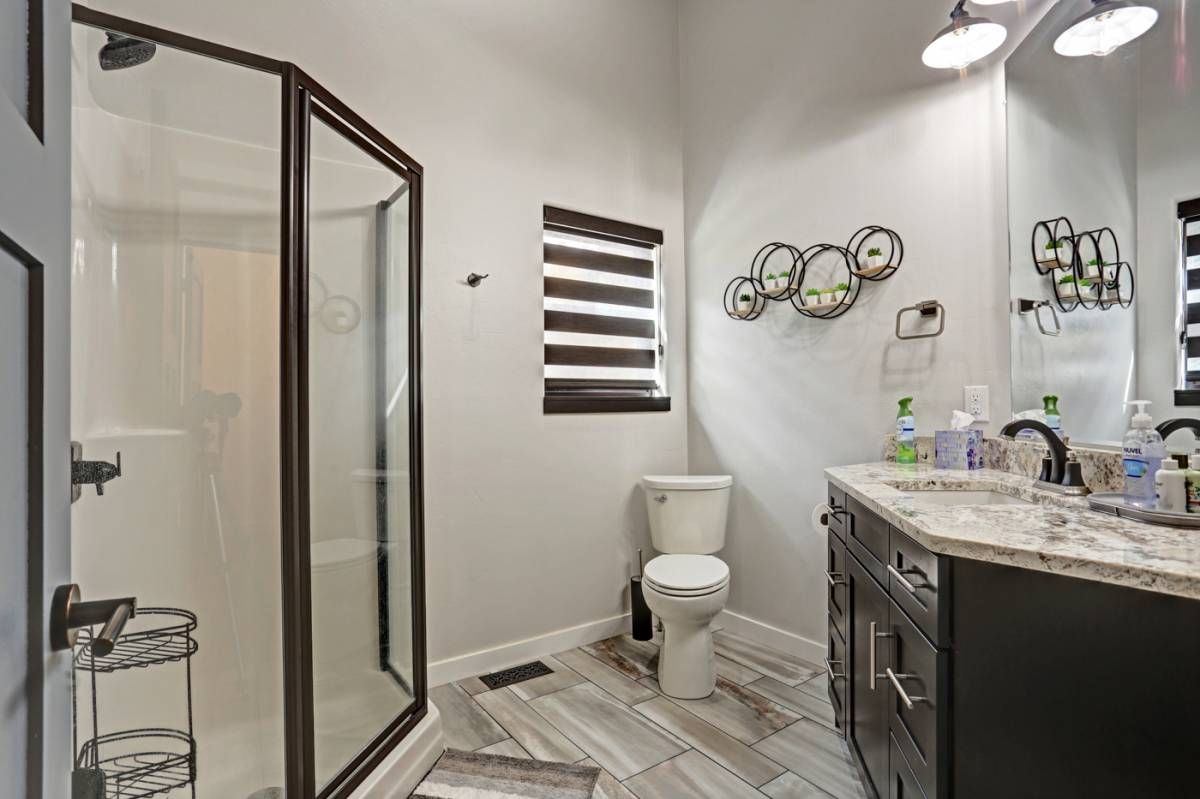 corner glass shower on left with dark cabinet vanity and white toilet on right