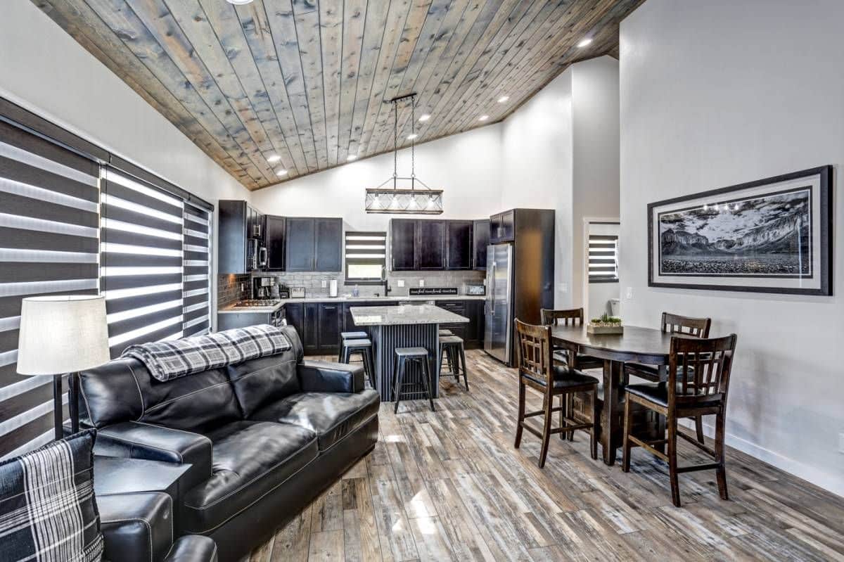 black sofa against left wall of living room with table on right and kitchen in background