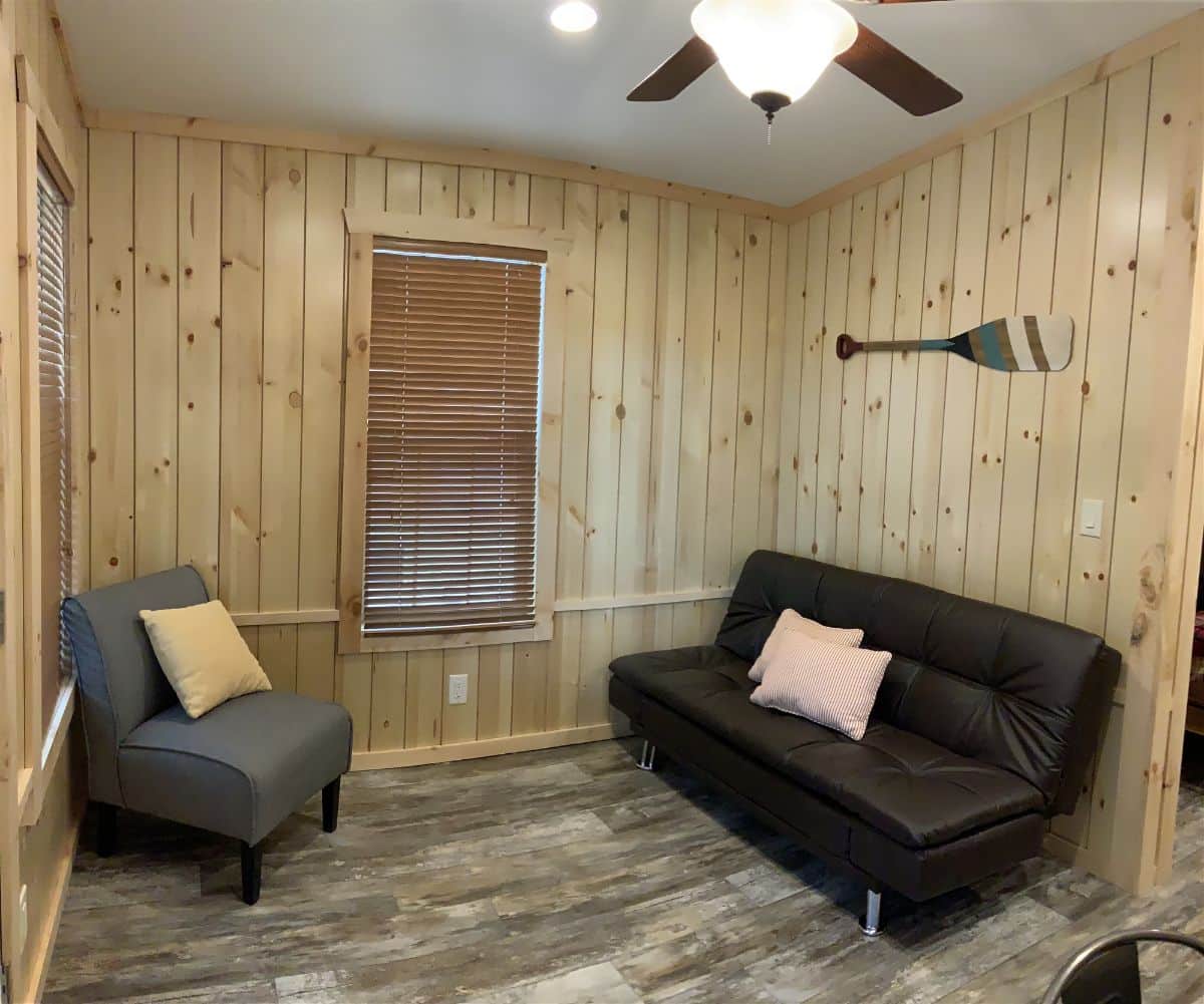 wood paneling on walls with black futon and gray chair