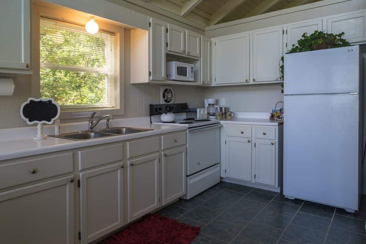 white cabinets and appliancesi n kitchen with gray floor and red rug