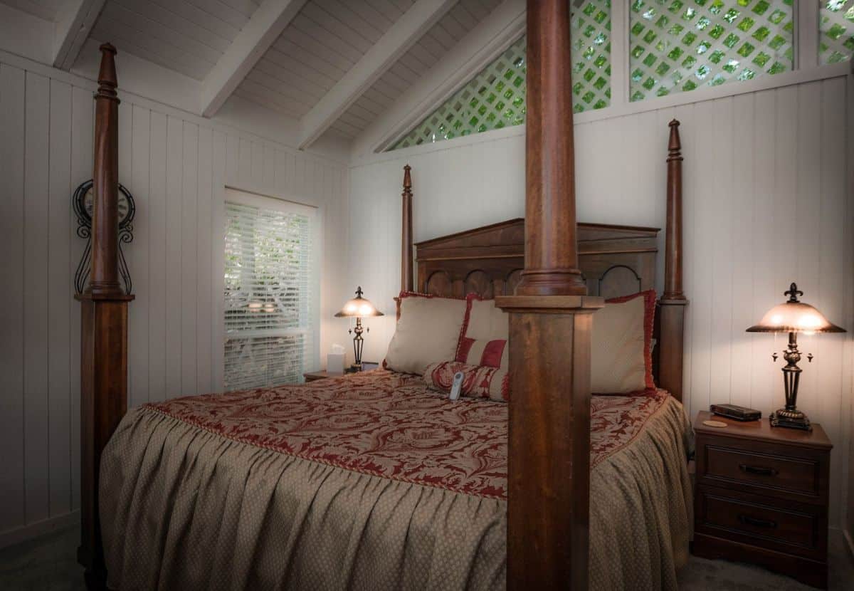 four poster bed against white walls in bedroom with windows above bed