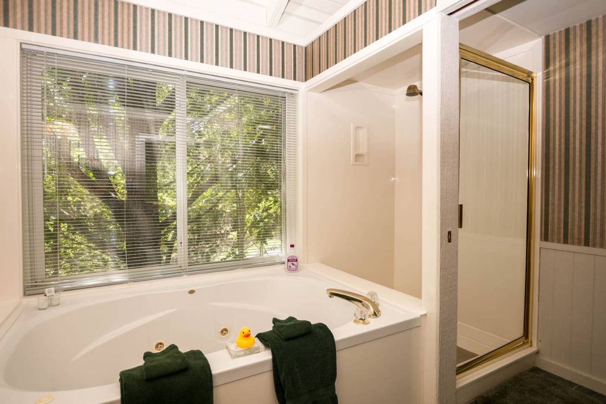 white soaking tub against picture window with glass door shower on right