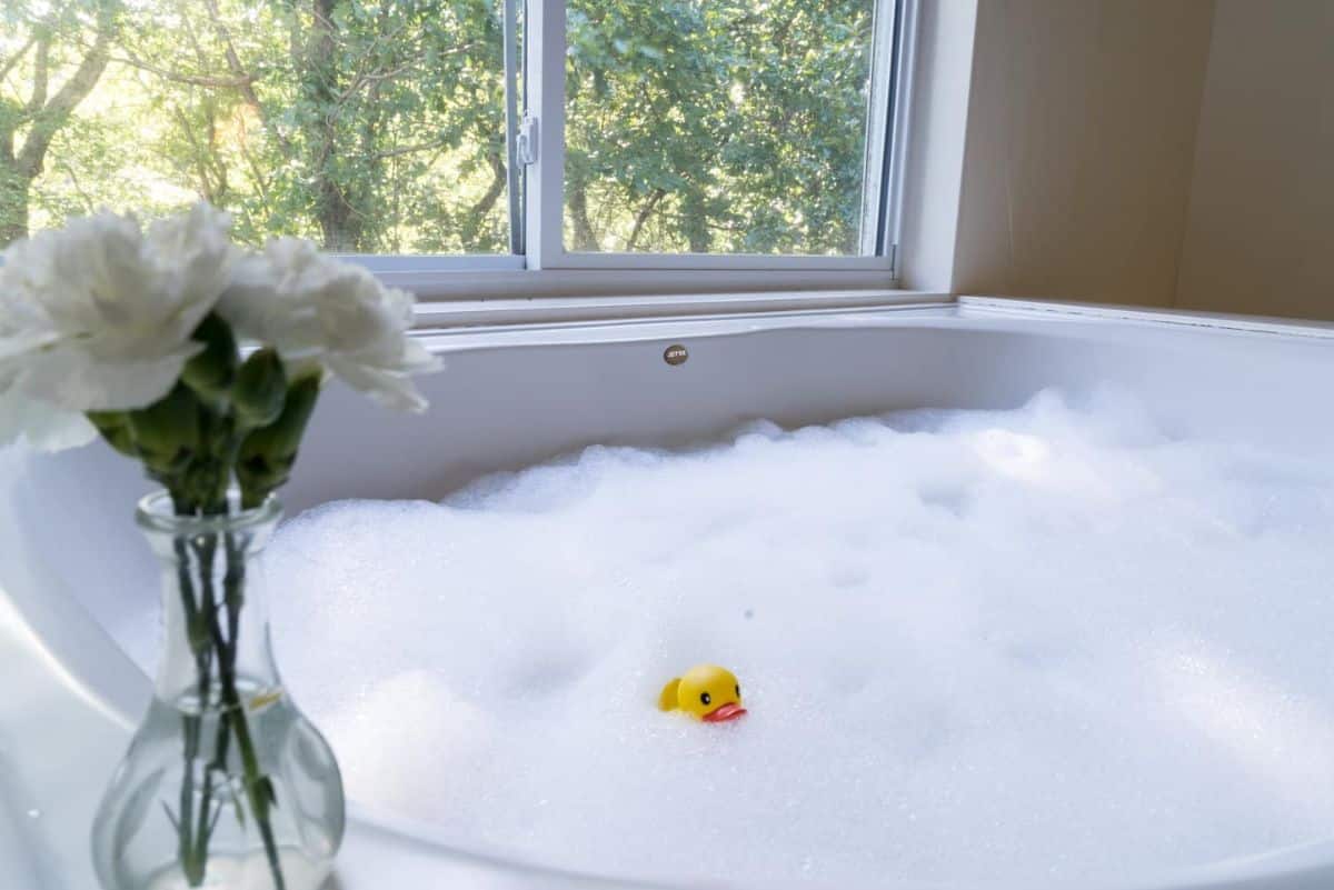 soaking tub full of bubbles with a vase and white carnations on the left and a rubber ducky in the bubbles