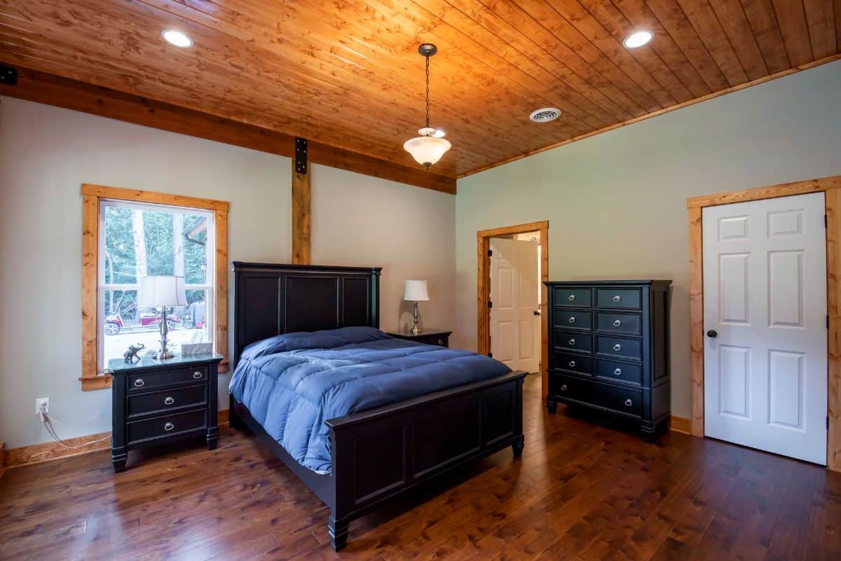 blue bedding on black bed in room with light green walls and windows behind bed