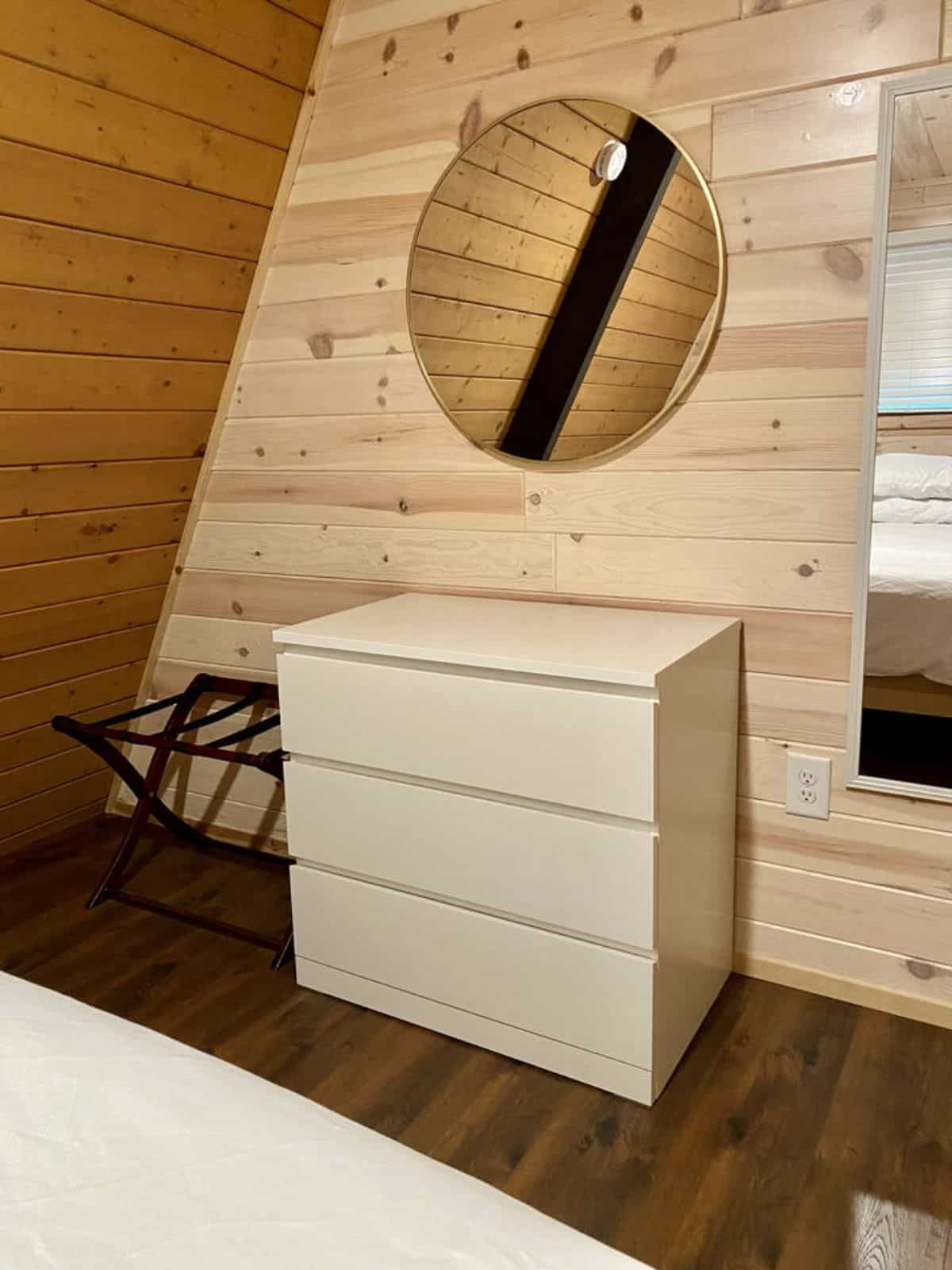 white chest of drawers below round mirror against wood wall