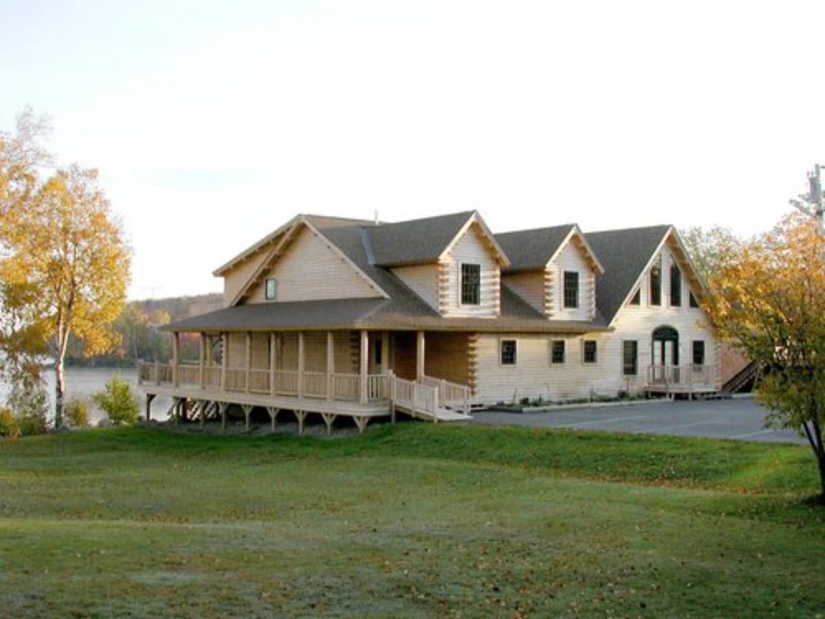 light wood cabin with dormer windows and paved driveway