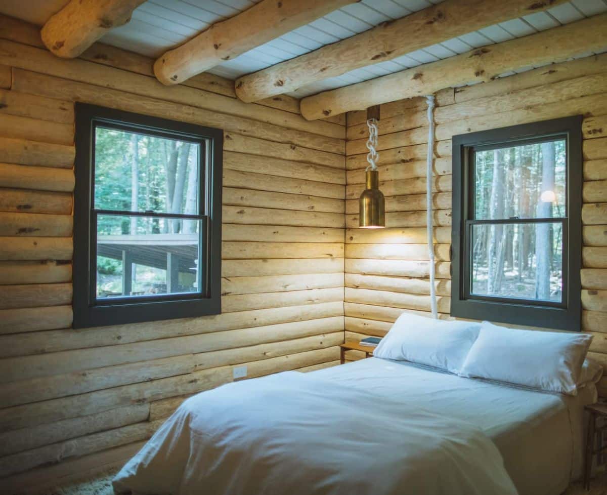 white bedding on bed under black trimmed window in cabin