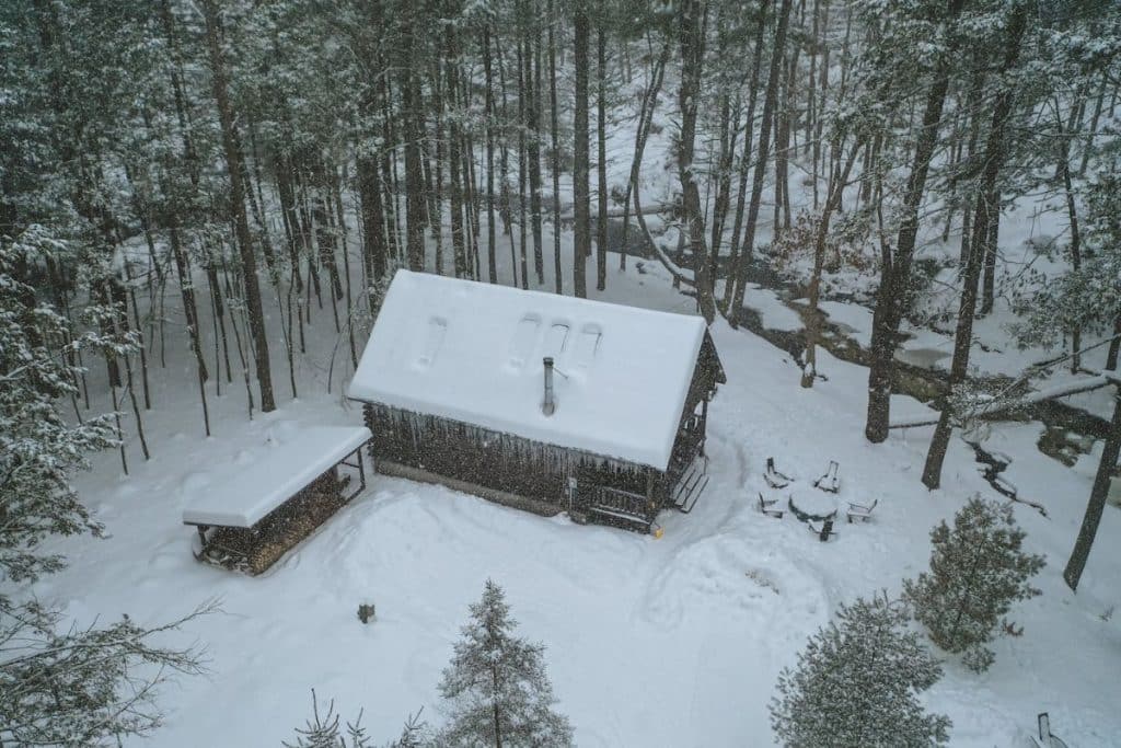 cabin in empty lot covered in snow with trees in background