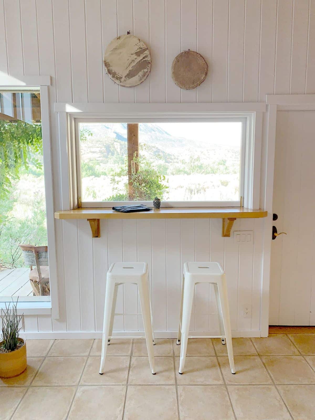 white bench beneath window with two white stools under bench