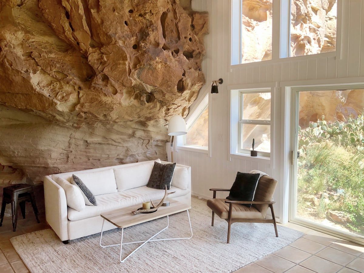 white sofa against rock outcropping with small chair beside open door