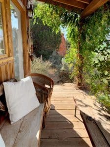 bench with white pillow on porch of cabin with green tree at end of porch