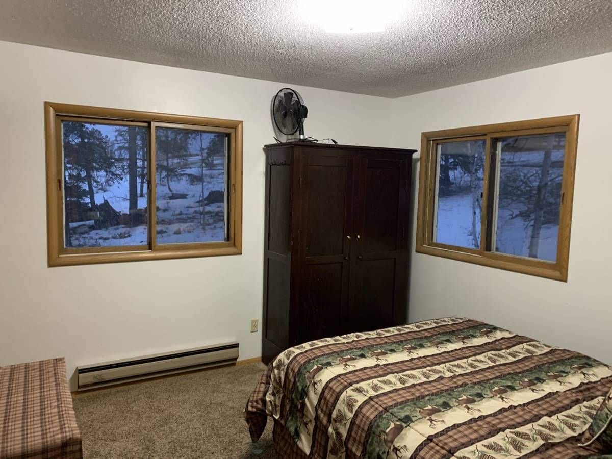 two windows on walls in bedroom with dark striped linens on bed