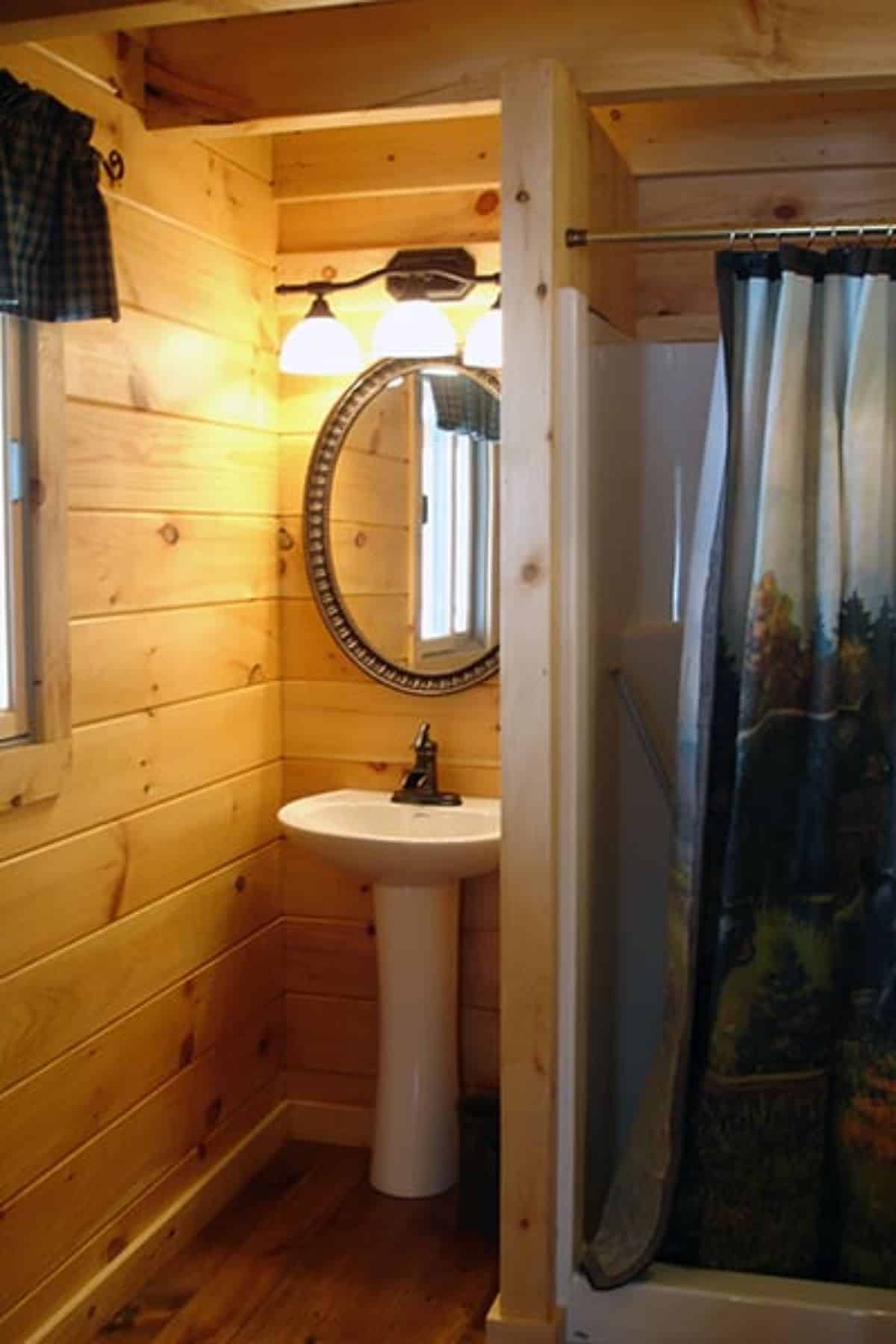 small cabin bathroom with shower on right and pedestal sink on left