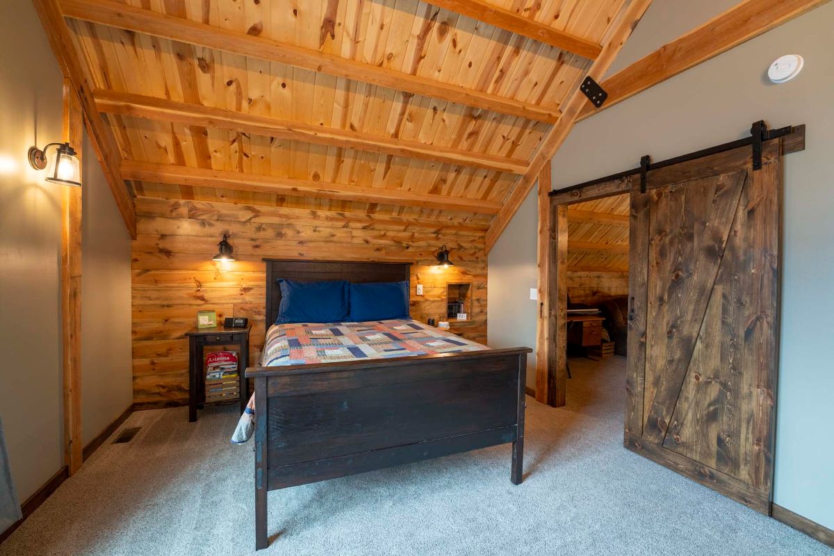 wood bed with quilt against wall in loft bedroom with barn door on right