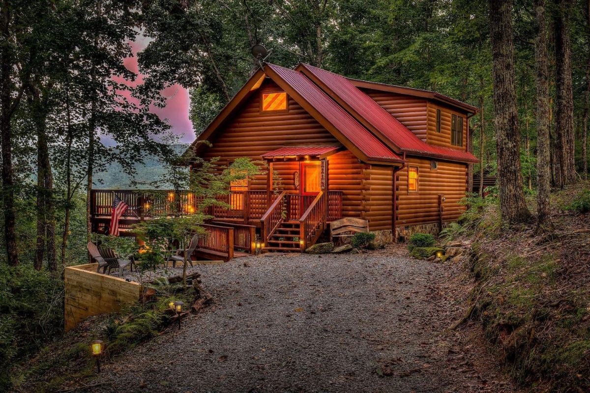 cabin on hill with lights on and gravel drive